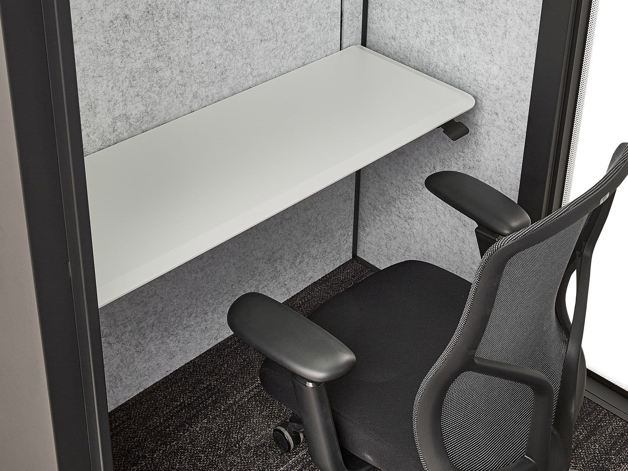 Inside an MW-Pod, showing the white wall-mounted sit-stand desk and black mesh office chair