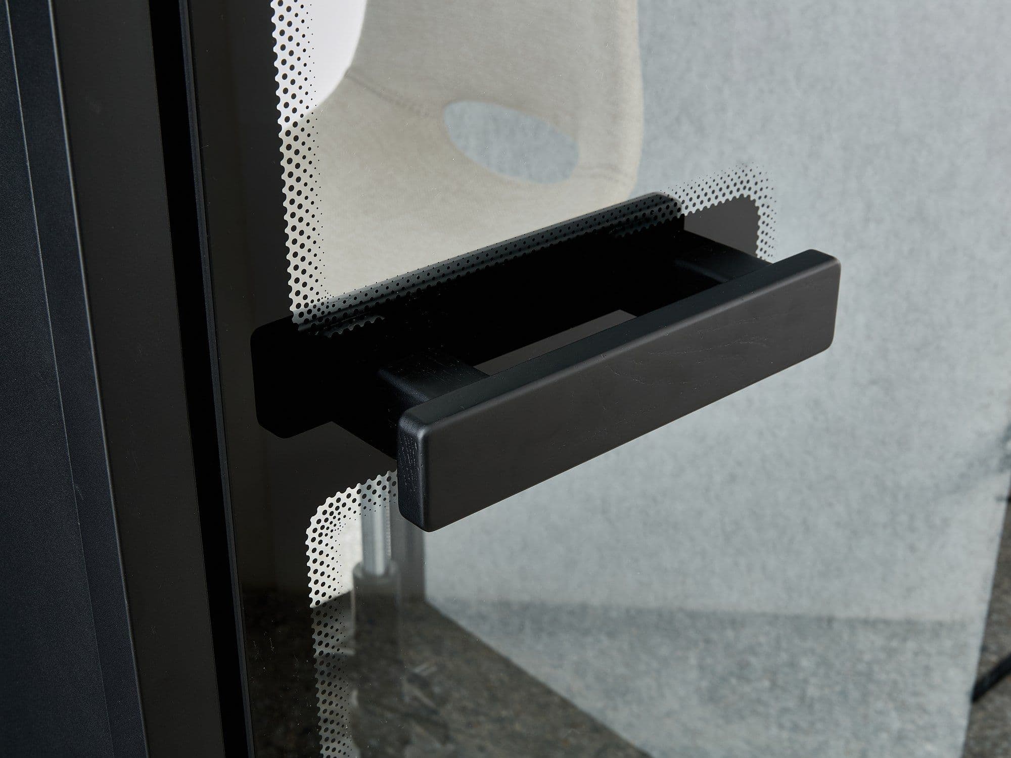 The black pull handle on a Peacepod glass door, against the grey acoustic felt interior